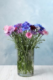 Photo of Bouquet of beautiful cornflowers in glass vase on white wooden table