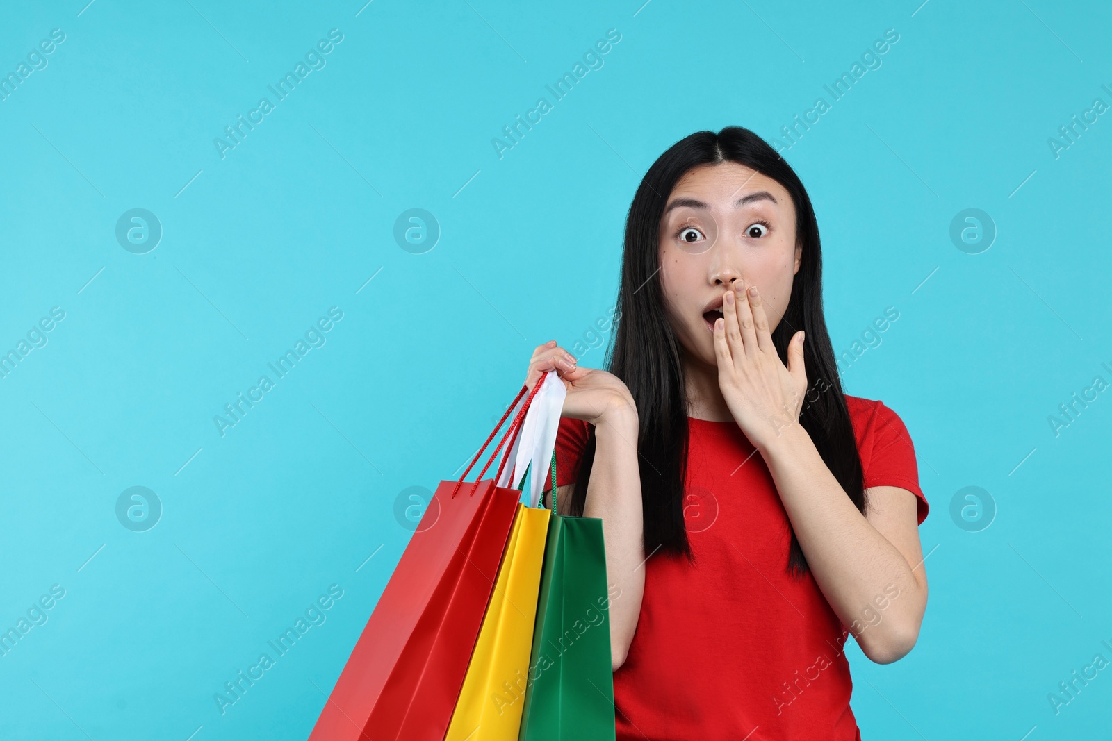 Photo of Surprised woman with shopping bags on light blue background. Space for text