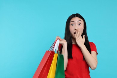 Photo of Surprised woman with shopping bags on light blue background. Space for text