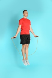 Full length portrait of young sportive man training with jump rope on color background