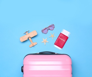 Photo of Pink suitcase and beach objects on blue background, flat lay