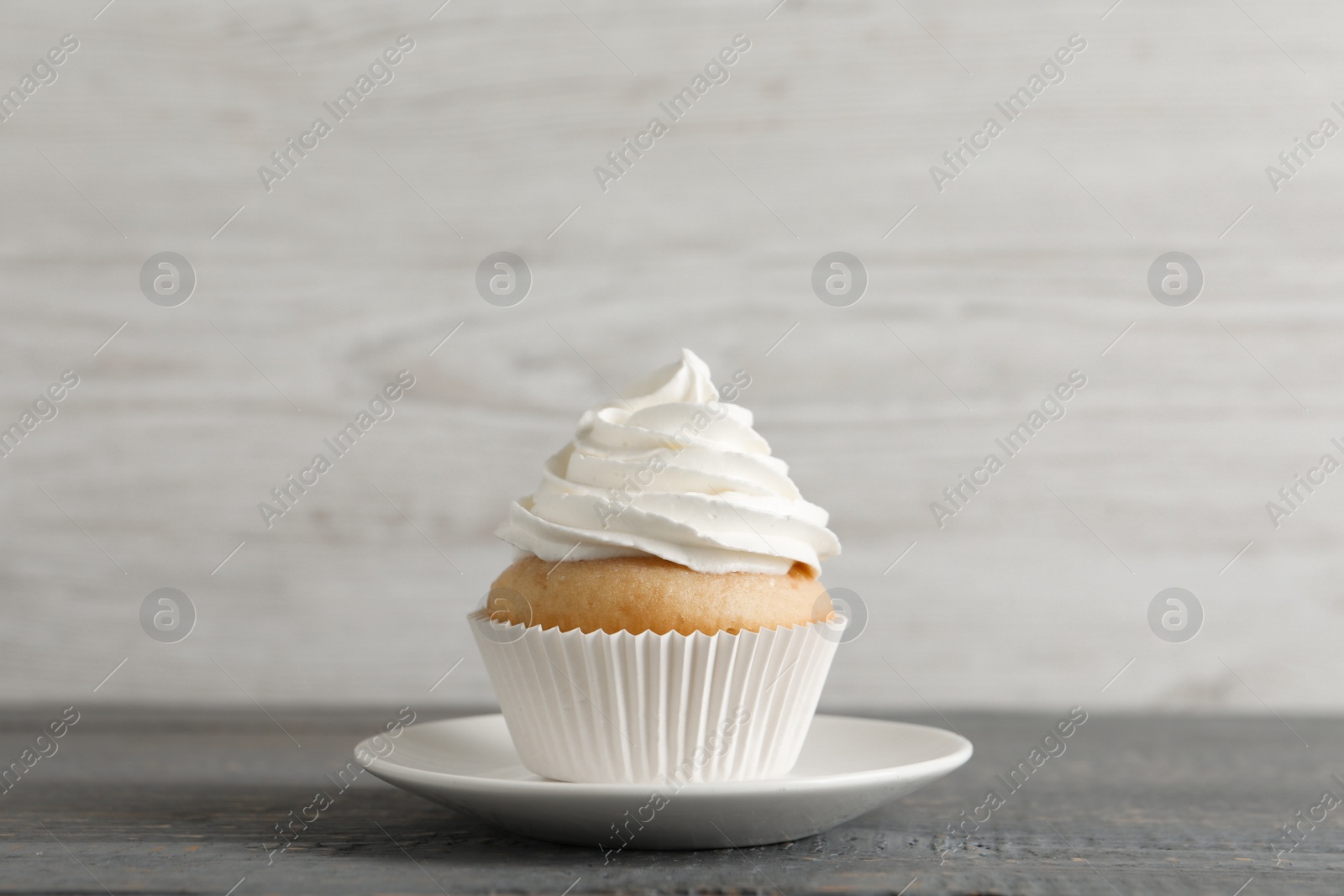 Photo of Delicious cupcake with cream on grey wooden table