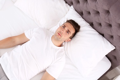 Photo of Young man lying in bed at home, top view. Sleep disorder