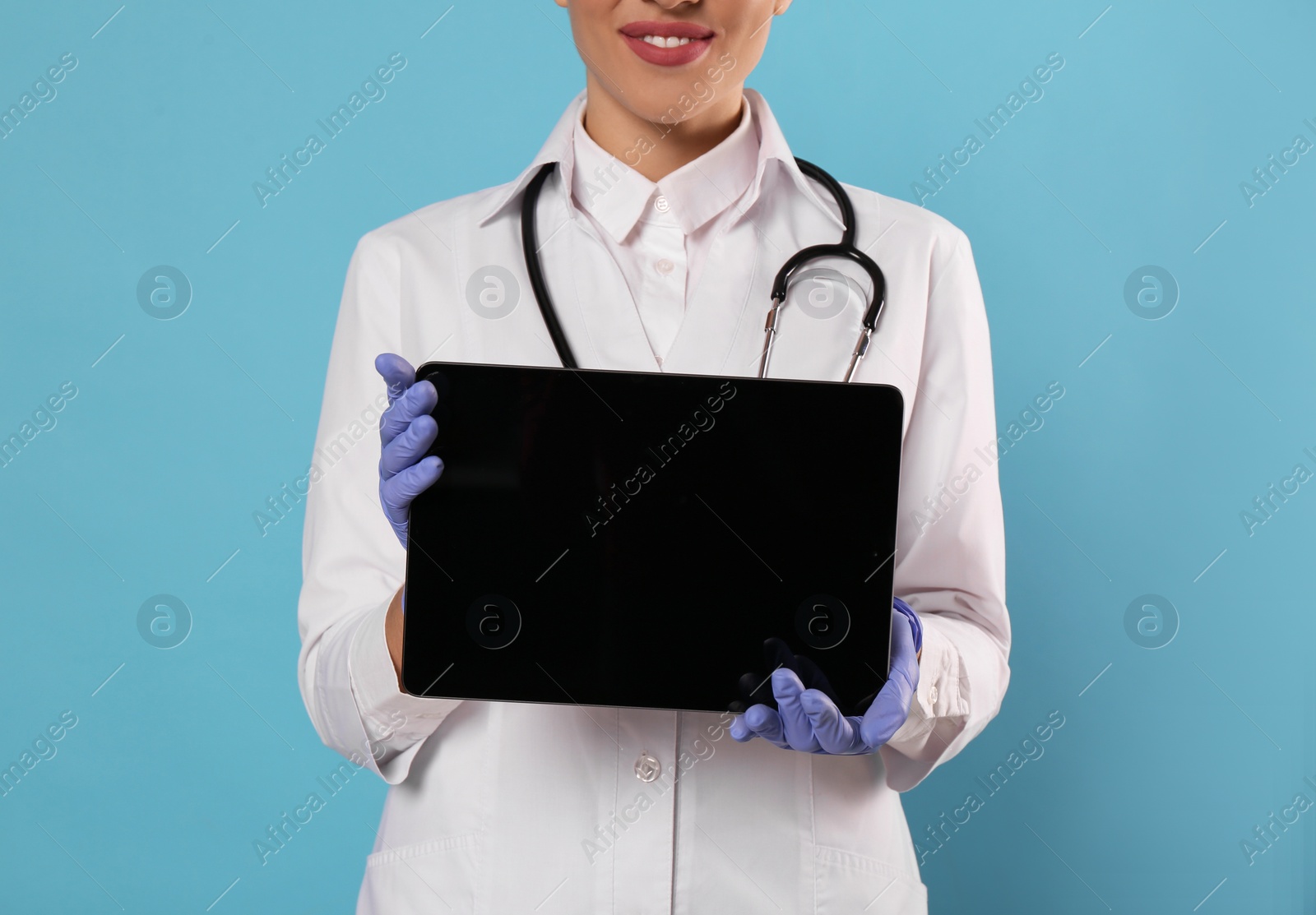 Photo of Closeup view of doctor with stethoscope holding blank tablet on light blue background, space for design. Cardiology concept