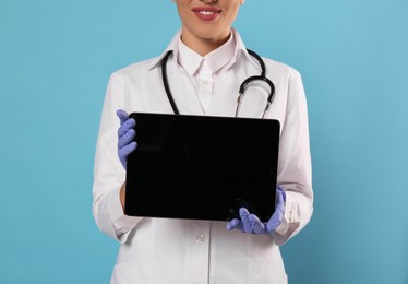 Photo of Closeup view of doctor with stethoscope holding blank tablet on light blue background, space for design. Cardiology concept