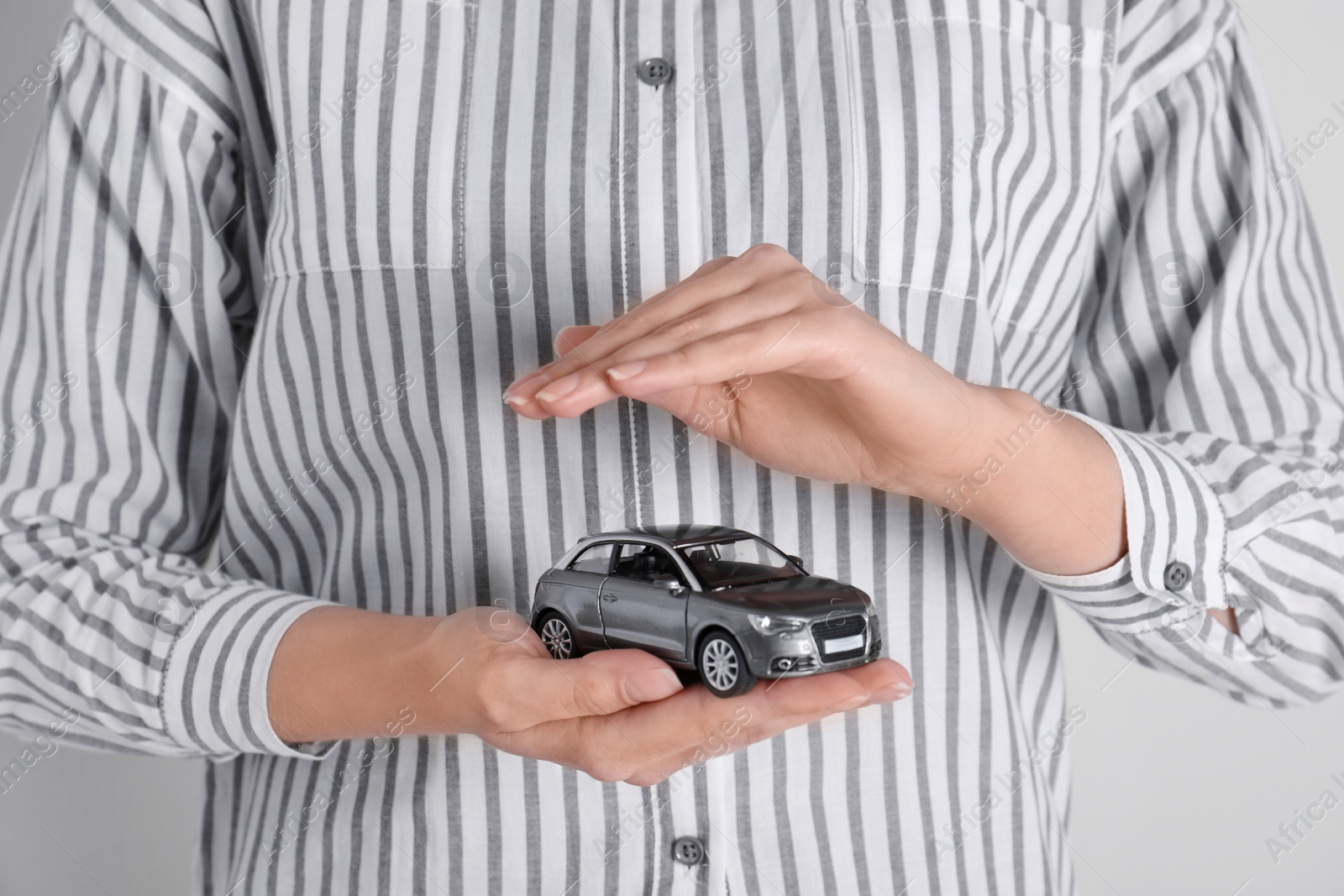 Photo of Insurance agent covering toy car on grey background, closeup