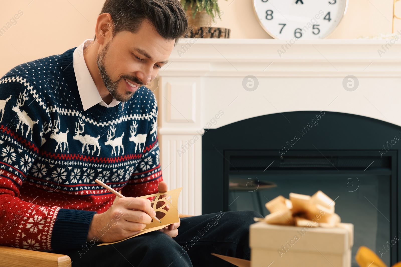 Photo of Happy man writing wishes in Christmas greeting card in living room