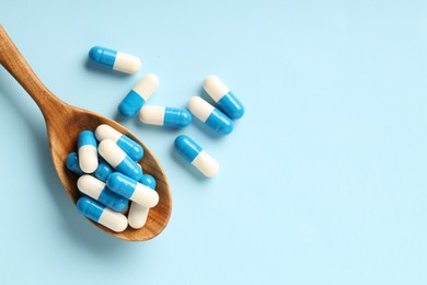 Antibiotic pills and spoon on light blue background, top view. Space for text