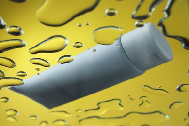 Moisturizing cream in tube on glass with water drops against yellow background