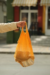 Photo of Conscious consumption. Woman with net bag of eco friendly products on city street, closeup