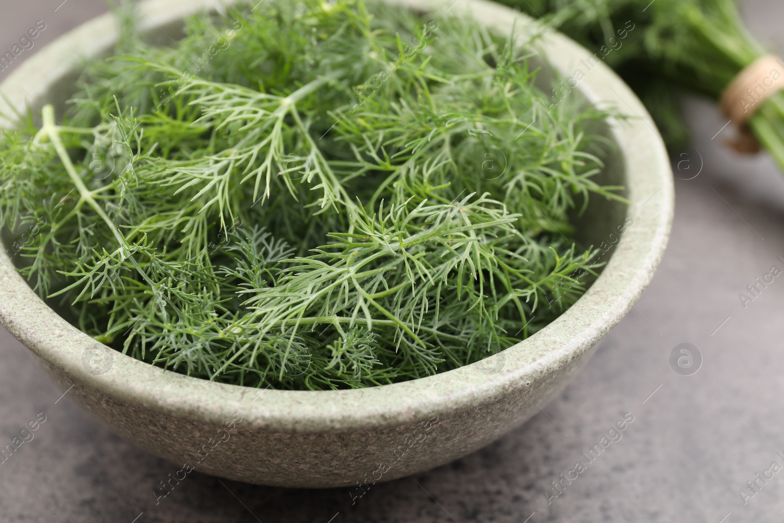 Photo of Bowl of fresh dill on grey table, closeup