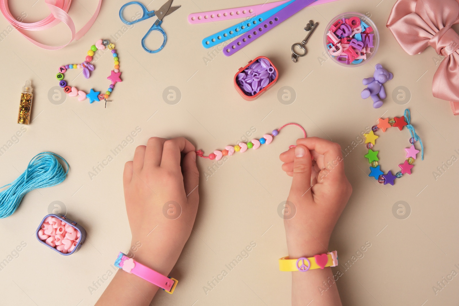 Photo of Child making beaded jewelry and different supplies on beige background, top view. Handmade accessories