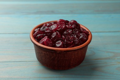Photo of Tasty dried cranberries in bowl on light blue wooden table, closeup