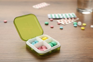 Plastic box with different pills on wooden table