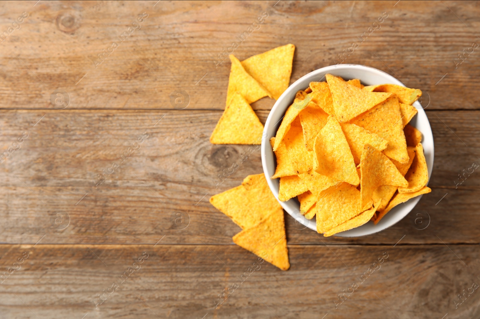 Photo of Tasty mexican nachos chips in bowl on wooden table, flat lay. Space for text