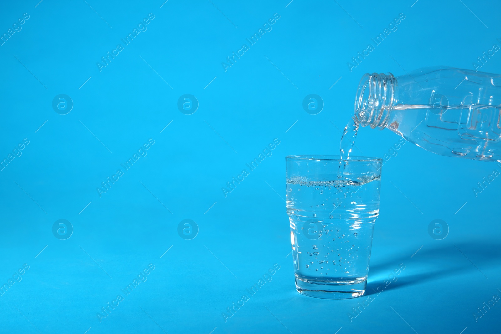 Photo of Pouring water from bottle into glass on blue background. Space for text