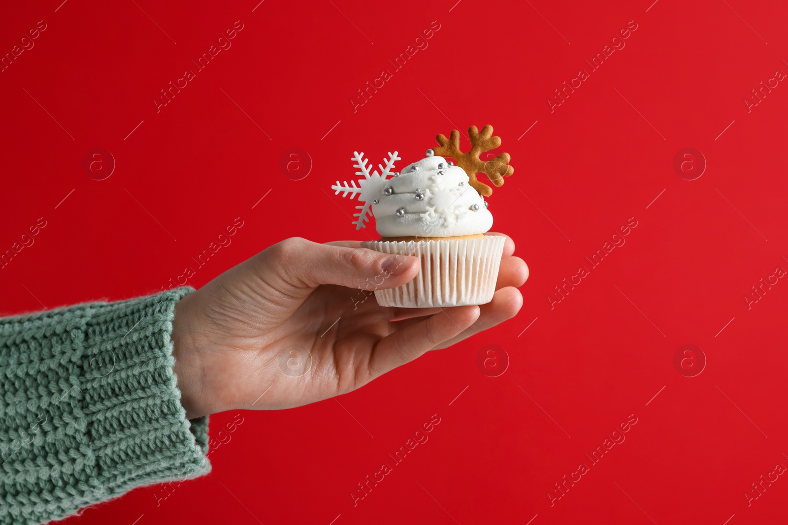 Photo of Woman holding tasty Christmas cupcake with cream and snowflake cookies on red background, closeup. celebration