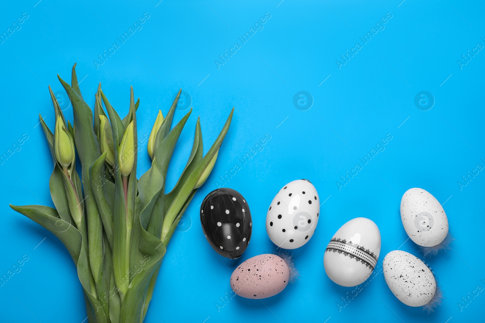 Photo of Flat lay composition with tulips and eggs on light blue background, space for text. Easter celebration