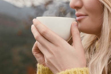 Photo of Young woman with cup of hot drink outdoors, closeup