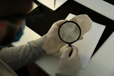 Photo of Detective with magnifying glass examining shoe sole print at table, closeup