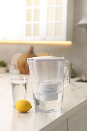 Water filter jug, glass and lemon on white marble table in kitchen