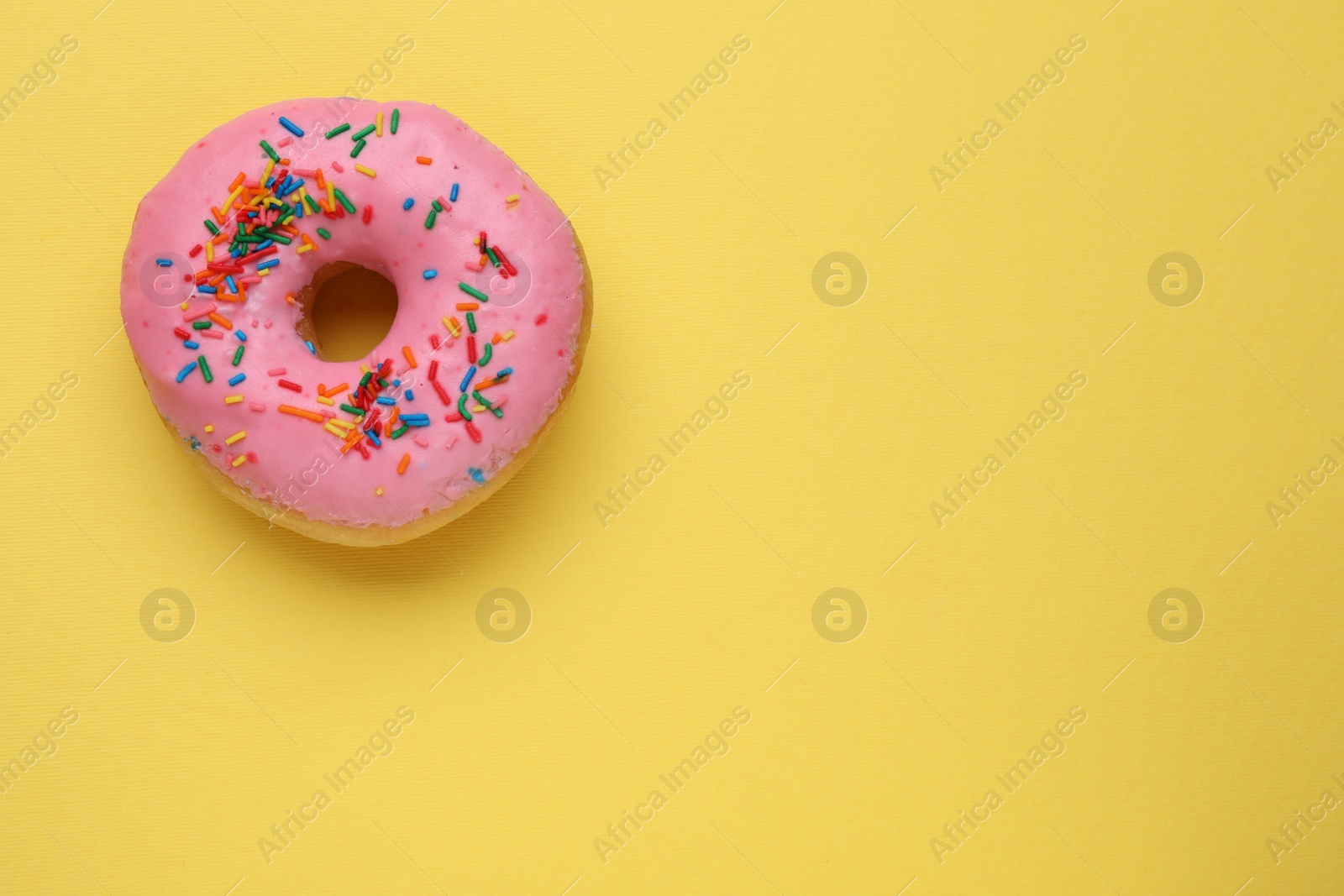 Photo of Tasty glazed donut decorated with sprinkles on yellow background, top view. Space for text