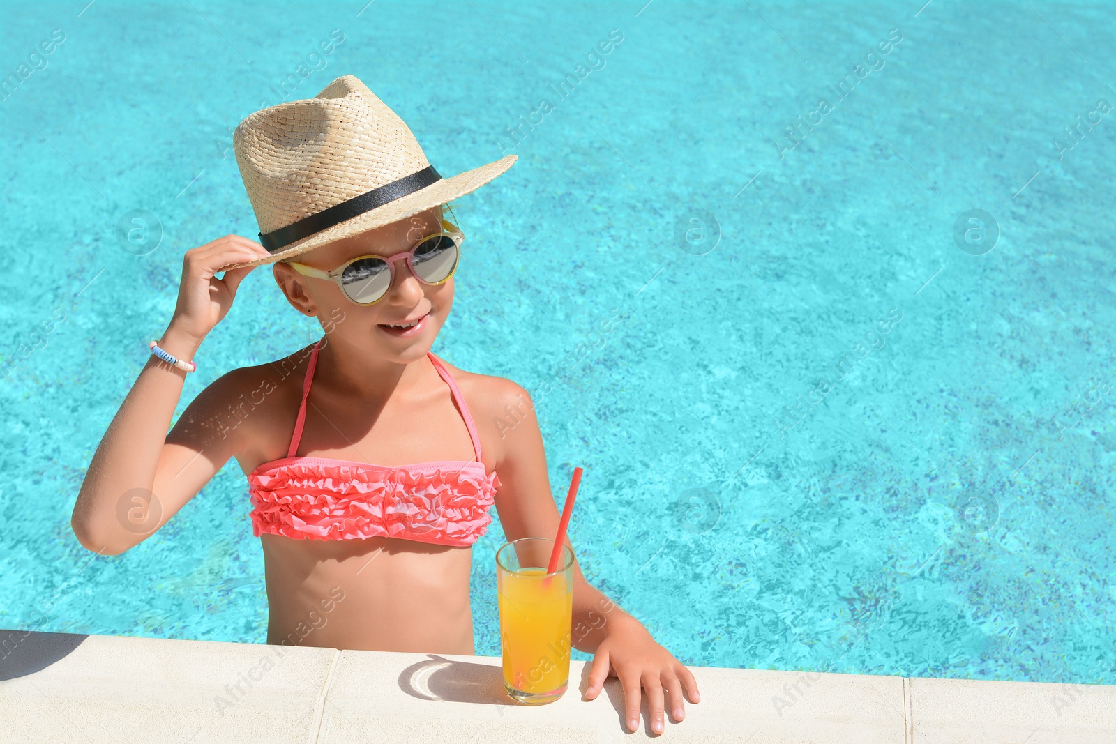 Photo of Cute little girl with glass of juice in swimming pool on sunny day. Space for text