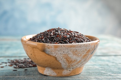 Bowl with uncooked black rice on wooden table