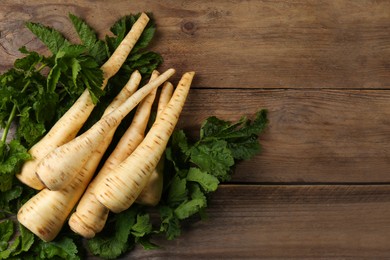 Fresh ripe parsnips with leaves on wooden table, flat lay. Space for text