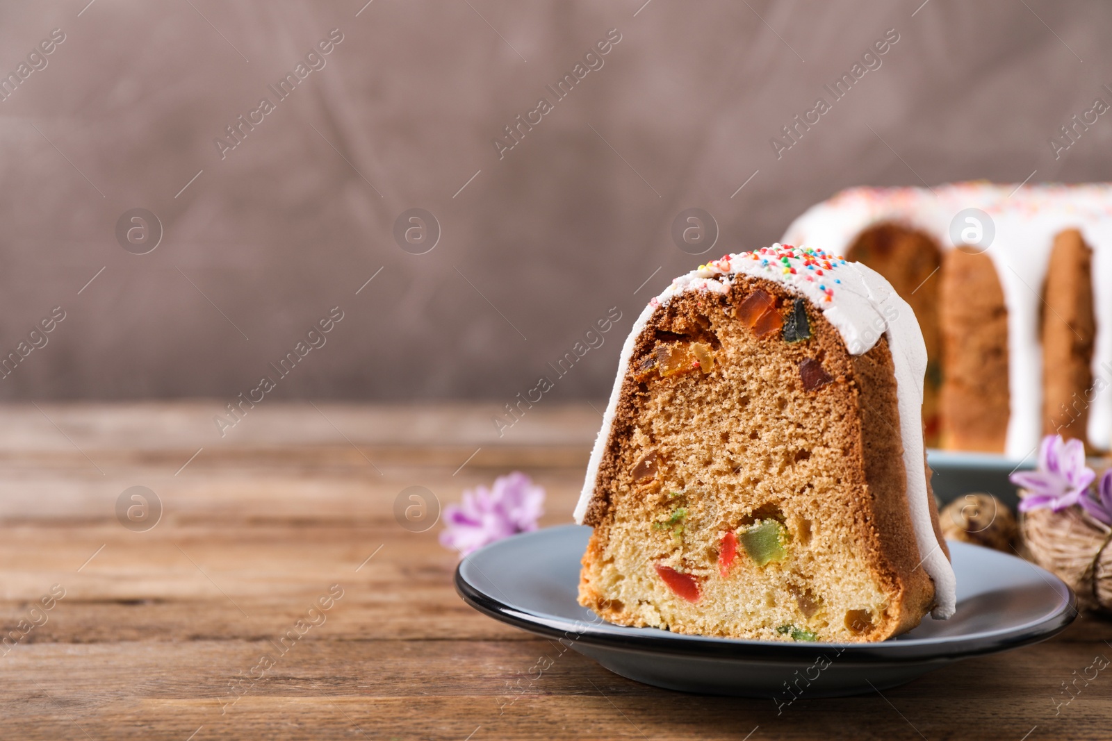 Photo of Piece of glazed Easter cake with sprinkles and candied fruits on wooden table, space for text