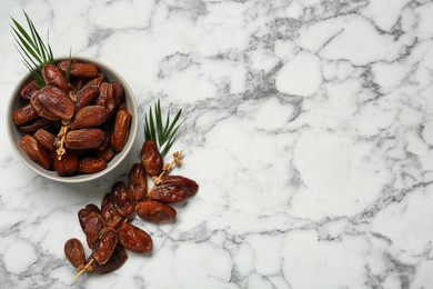 Photo of Tasty sweet dried dates and green leaves on white marble table, flat lay. Space for text