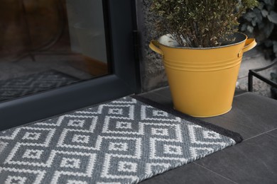 Stylish door mat and beautiful flowers near entrance