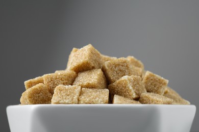 Photo of Brown sugar cubes in bowl on grey background, closeup