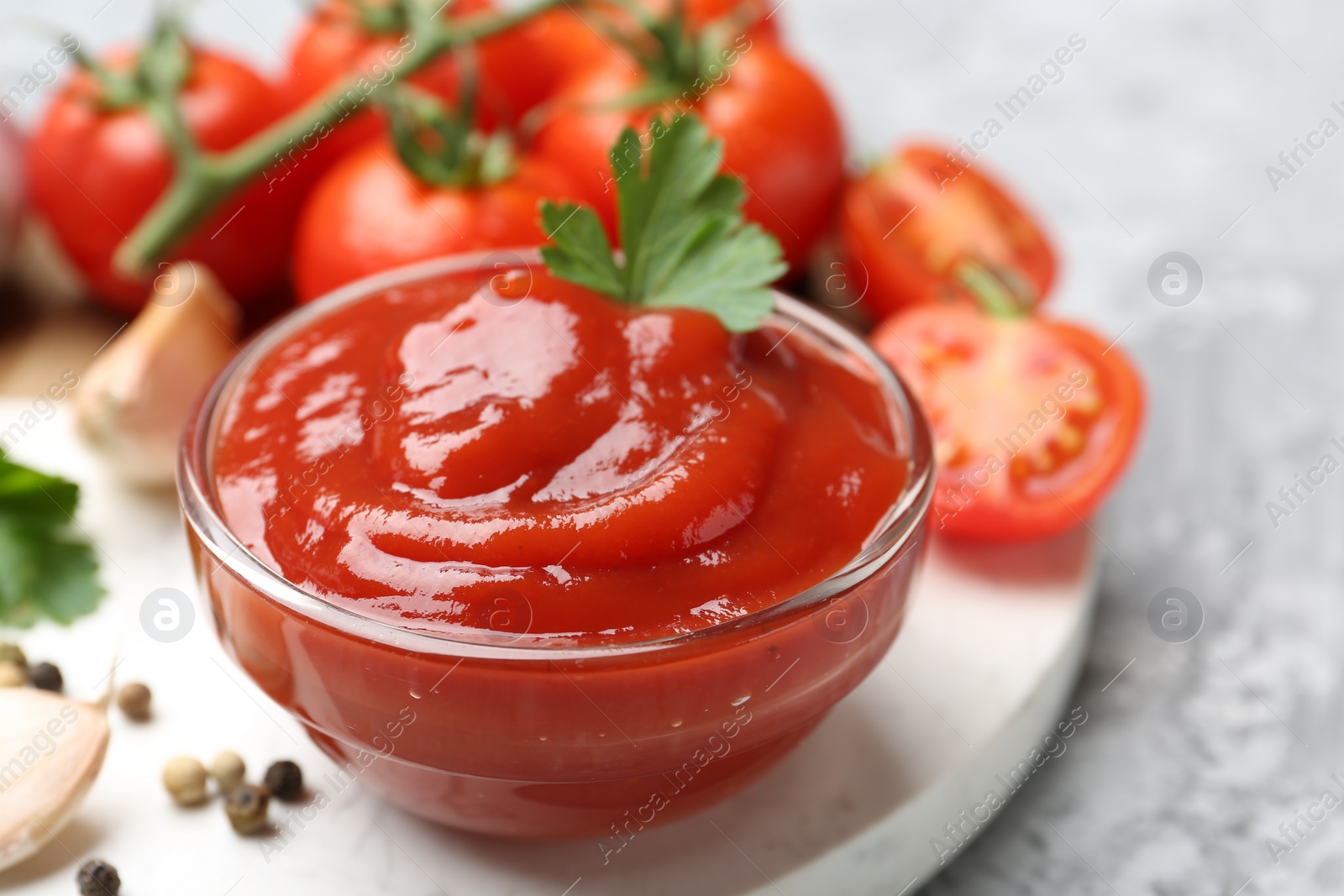 Photo of Delicious tomato ketchup and parsley in bowl on grey table, closeup