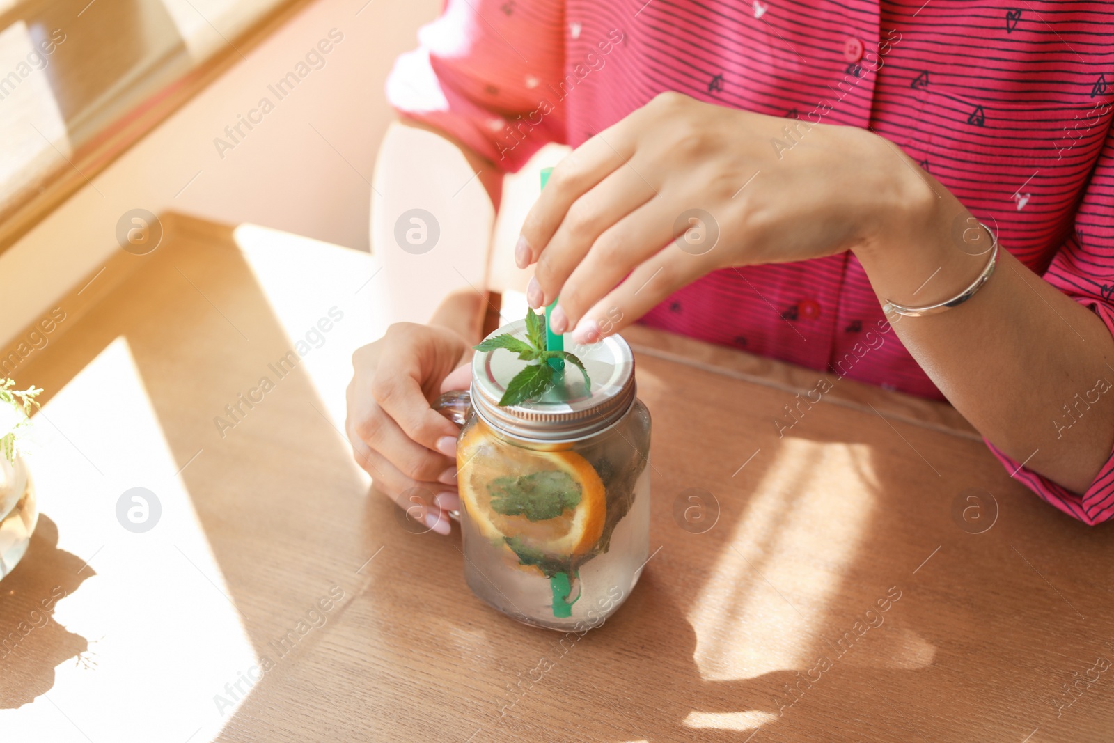 Photo of Young woman with mason jar of tasty natural lemonade in cafe, closeup. Detox drink