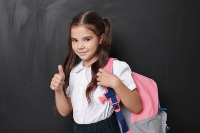Cute schoolgirl showing thumbs up near chalkboard