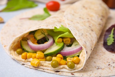 Photo of Delicious hummus wrap with vegetables on table, closeup