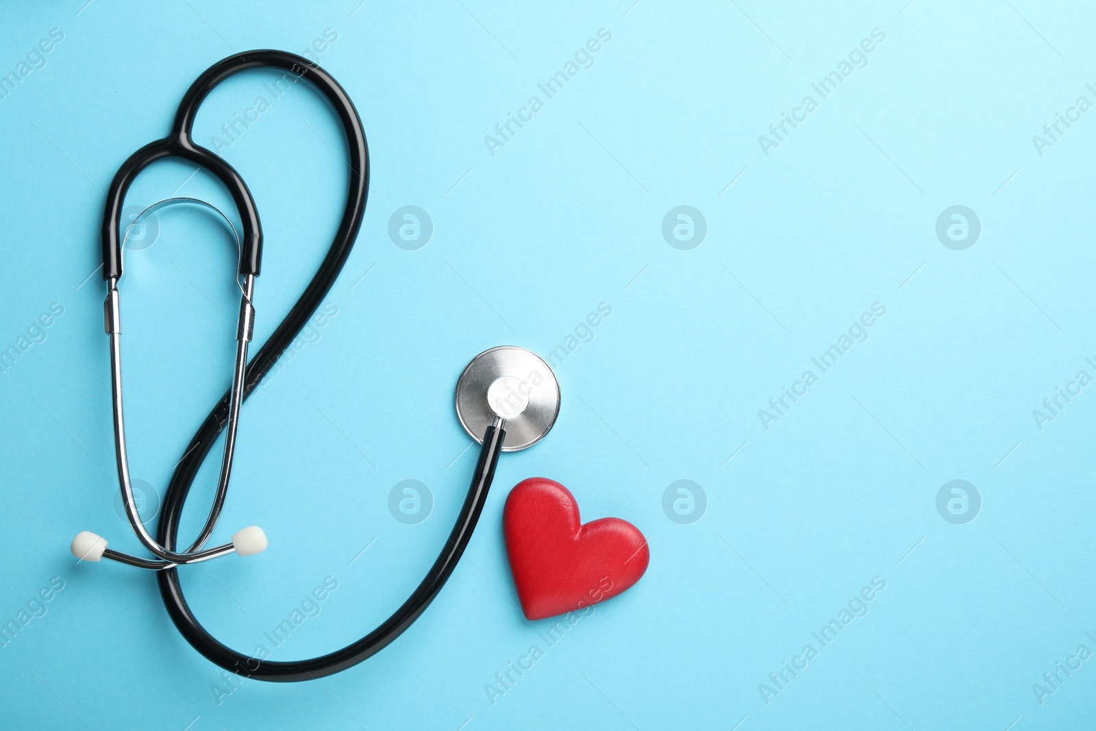 Photo of Stethoscope and red heart on light blue background, top view. Space for text