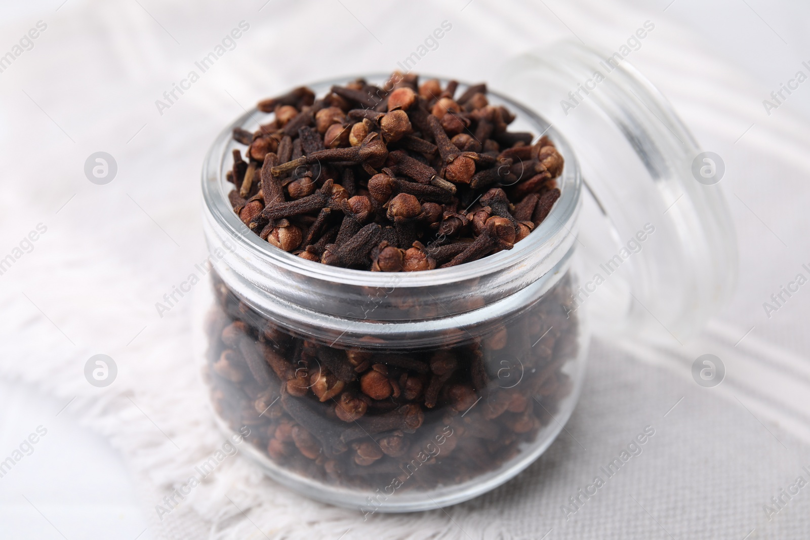 Photo of Aromatic cloves in glass jar on white table, closeup