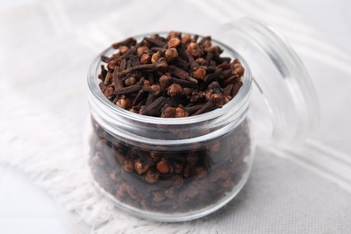 Aromatic cloves in glass jar on white table, closeup