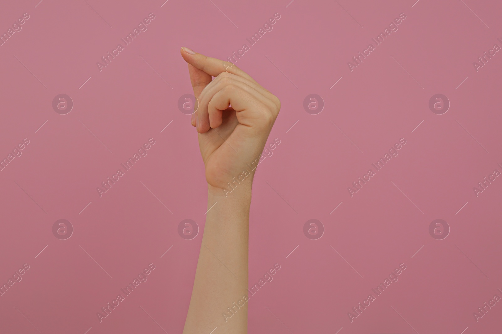 Photo of Woman showing thumb and index finger together on pink background, closeup