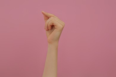 Photo of Woman showing thumb and index finger together on pink background, closeup