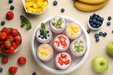 Photo of Yogurt maker with jars and different fruits on wooden table, flat lay