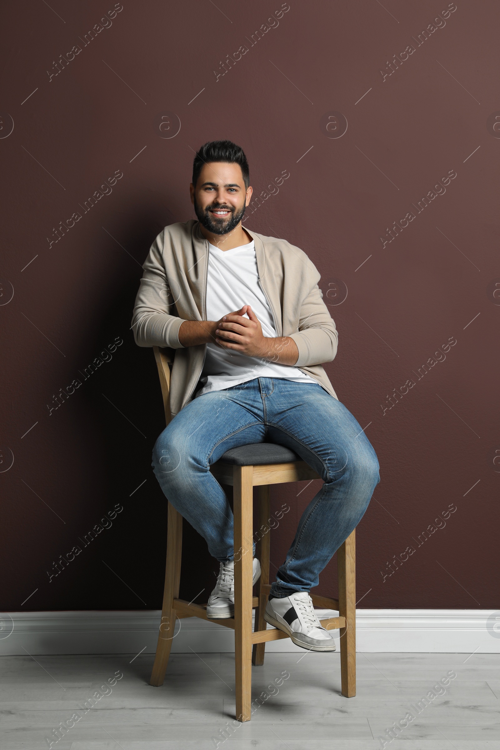 Photo of Handsome young man sitting on stool near brown wall