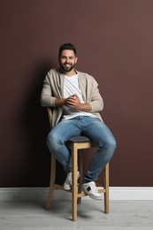 Handsome young man sitting on stool near brown wall