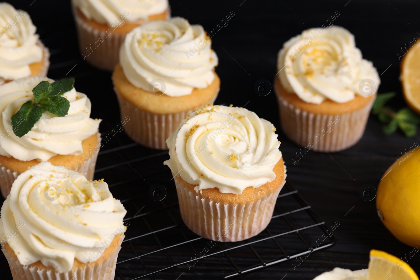 Photo of Delicious cupcakes with white cream and lemon zest on cooling rack, closeup