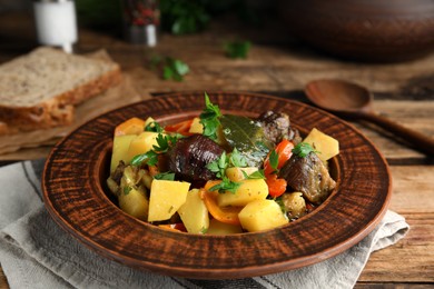 Photo of Tasty cooked dish with potatoes in earthenware served on wooden table