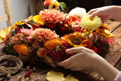 Florist making beautiful autumnal wreath with flowers and fruits at wooden table, closeup