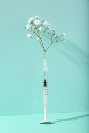 Photo of Cosmetology. Medical syringe and gypsophila on turquoise background
