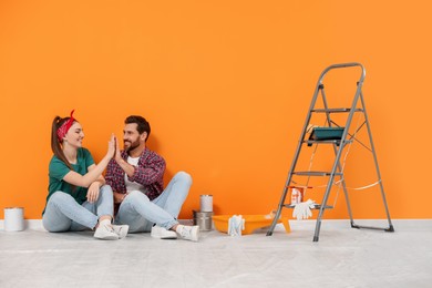 Photo of Designers giving high five on floor near freshly painted orange wall indoors